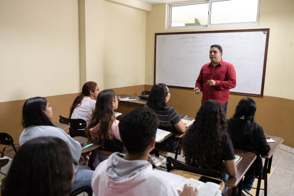 La imagen actual no tiene texto alternativo. El nombre del archivo es: profesor_estudiantes_salon_enclases_1-scaled.jpg
